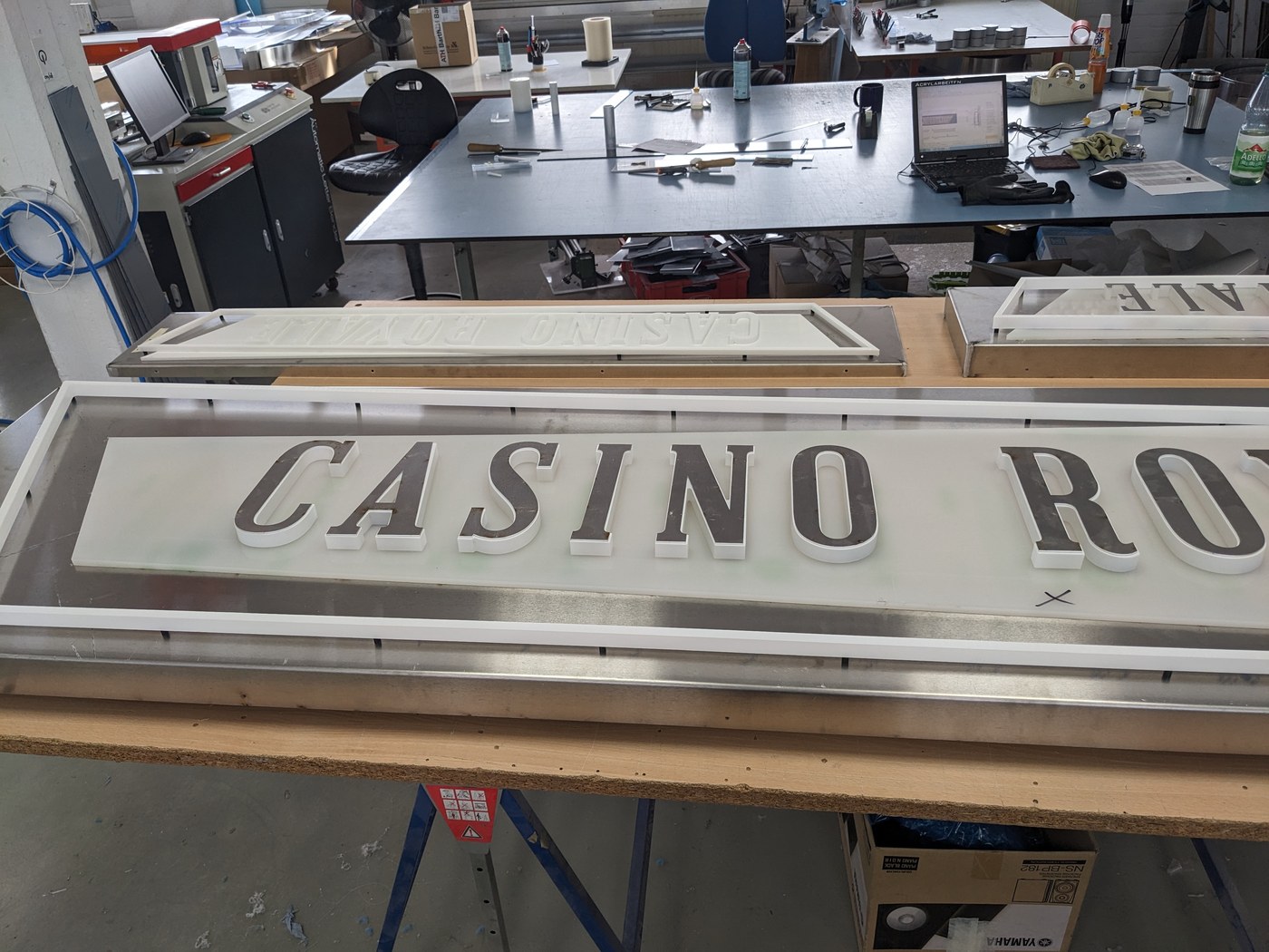 Casino Royale — weiße Acrylfront mit durchgesteckten Buchstaben auf der Werkbank